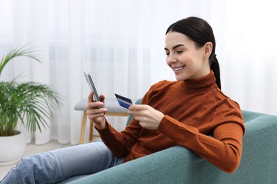 Happy young woman with smartphone and credit card shopping online on sofa at home