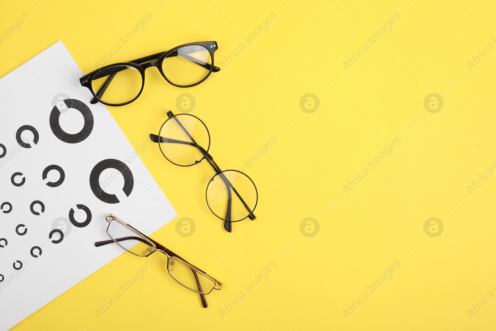 Photo of Vision test chart and glasses on yellow background, flat lay. Space for text