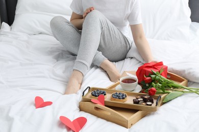 Photo of Tasty breakfast served in bed. Woman with desserts, tea and flowers at home, closeup