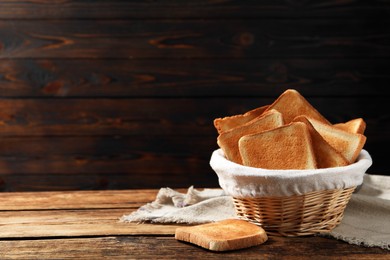 Slices of tasty toasted bread in wicker basket on wooden table, space for text