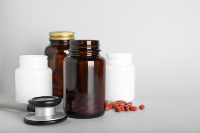 Photo of Bottles with pills and stethoscope on light background, space for text. Anemia treatment