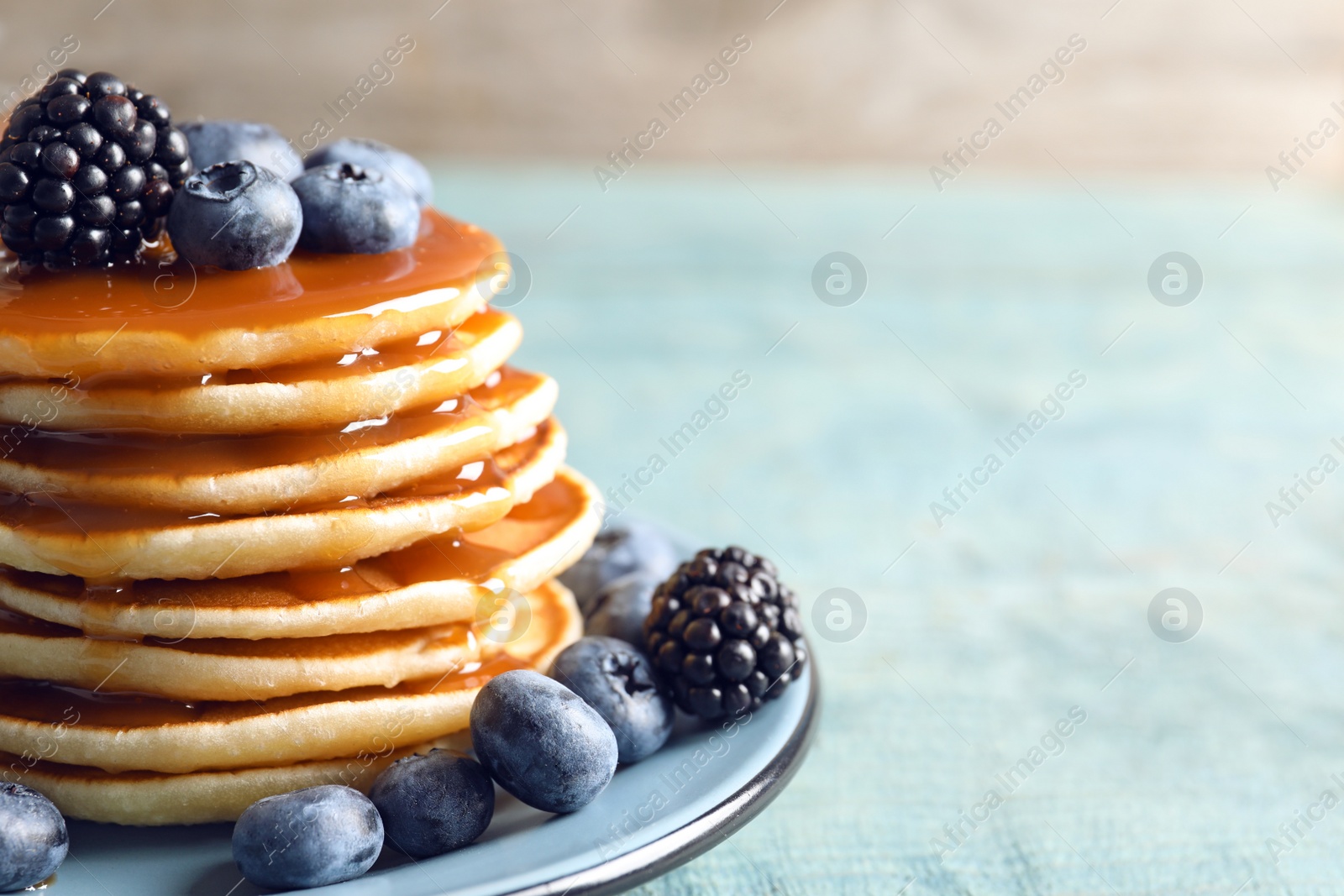 Photo of Tasty pancakes with berries and syrup on plate, closeup