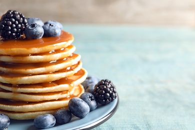 Photo of Tasty pancakes with berries and syrup on plate, closeup