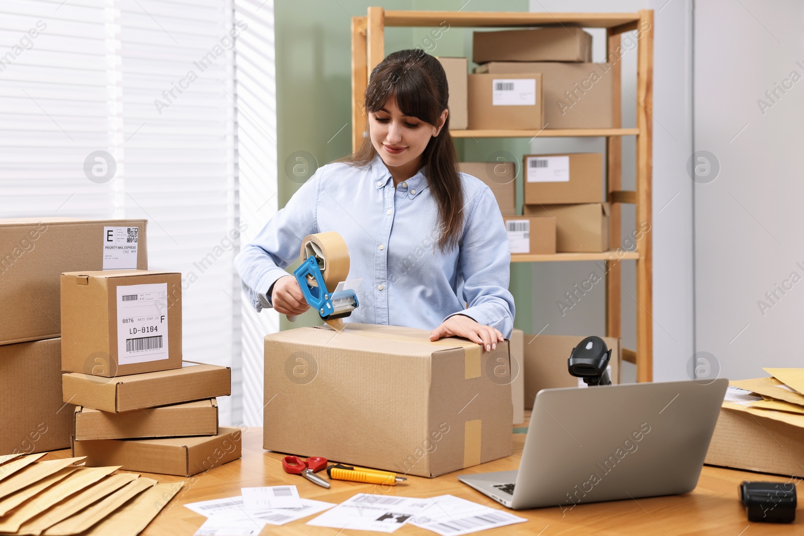 Photo of Parcel packing. Post office worker taping box at wooden table indoors