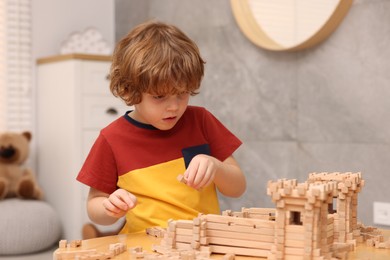 Photo of Little boy playing with wooden entry gate at table in room. Child's toy