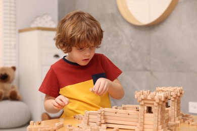 Little boy playing with wooden entry gate at table in room. Child's toy