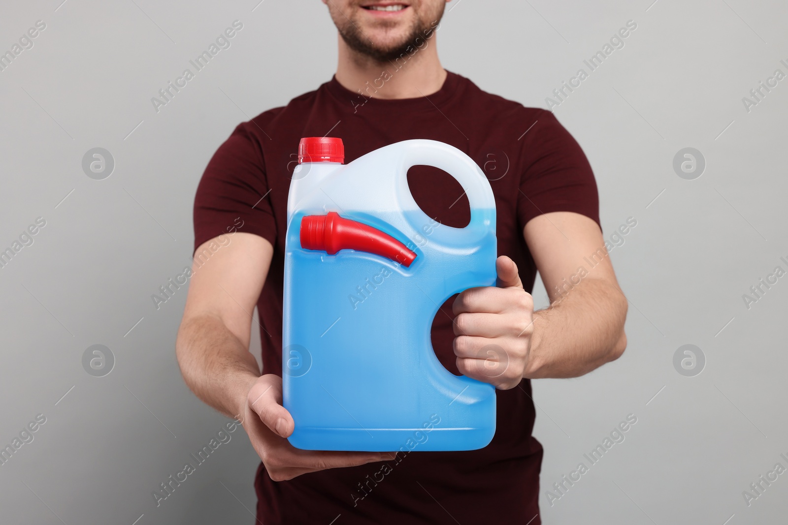 Photo of Man holding canister with blue liquid on light grey background, closeup