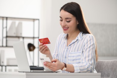 Photo of Woman with credit card using laptop and smartphone for online shopping indoors