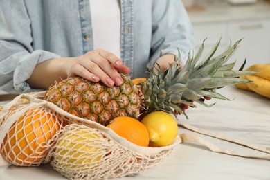 Photo of Woman with string bag of fresh fruits at light table, closeup