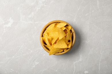 Photo of Tasty mexican nachos chips in wooden bowl on grey table, top view
