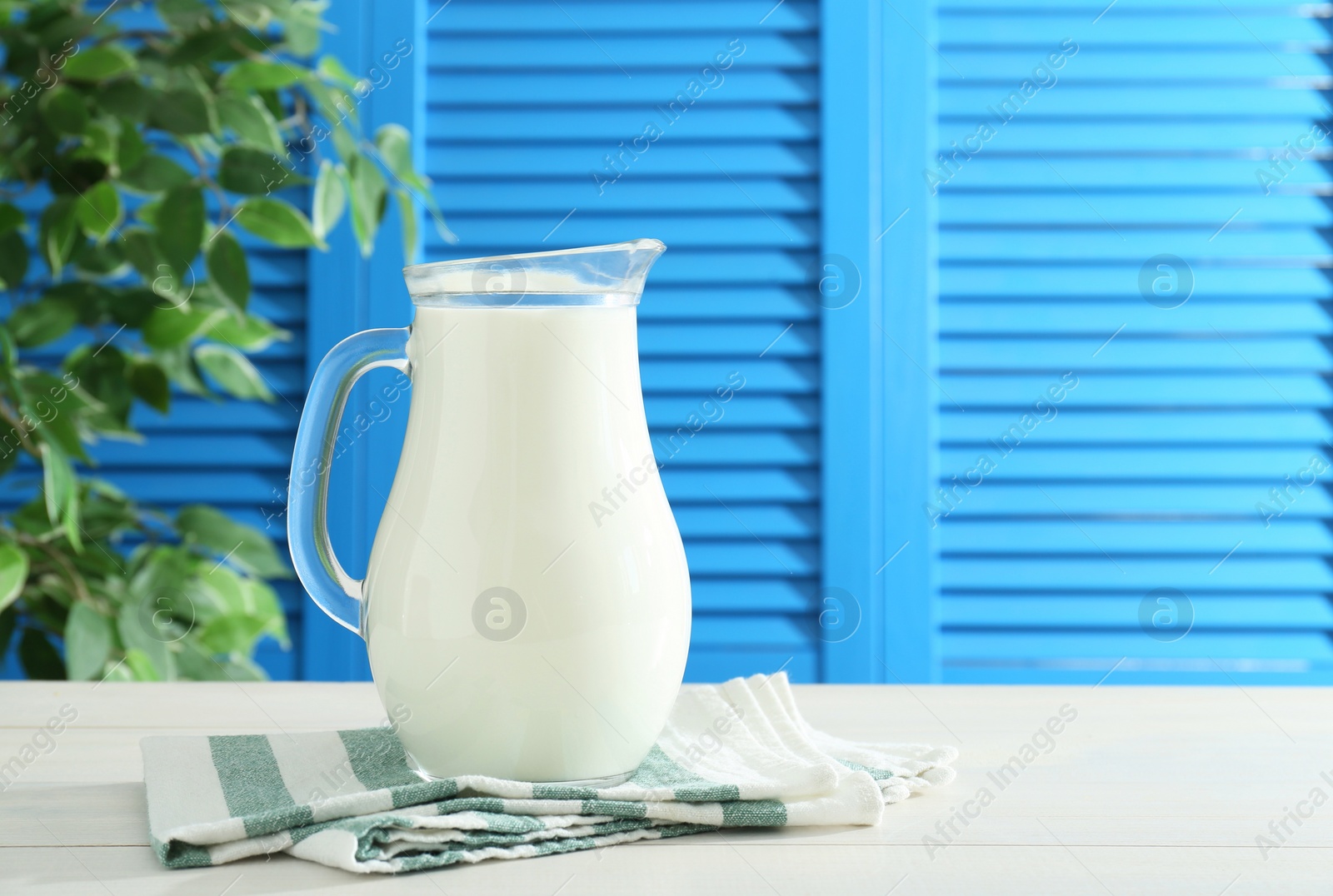 Photo of Jug of fresh milk on white wooden table, space for text