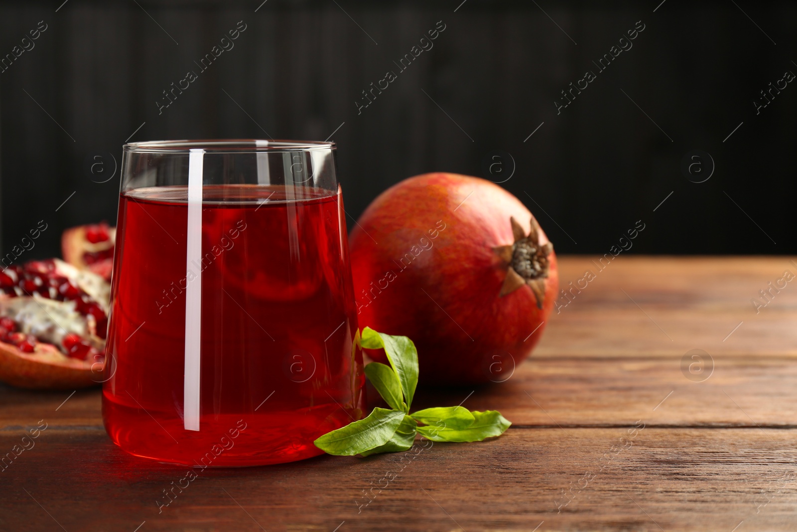 Photo of Tasty pomegranate juice in glass and fresh fruits on wooden table, closeup. Space for text