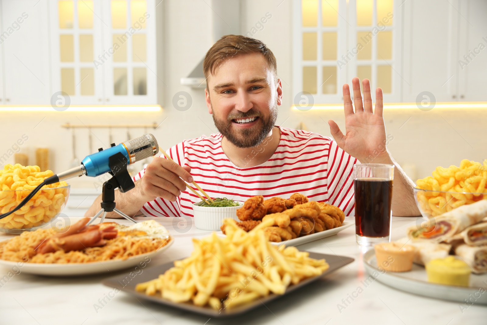 Photo of Food blogger recording eating show near microphone at table in kitchen. Mukbang vlog