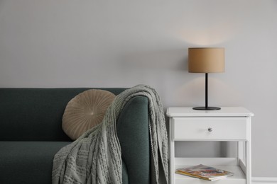 Photo of Stylish lamp on bedside table near sofa in room