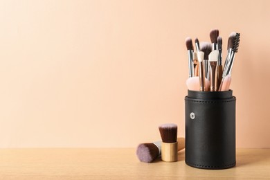 Photo of Set of professional makeup brushes on wooden table against beige background, space for text