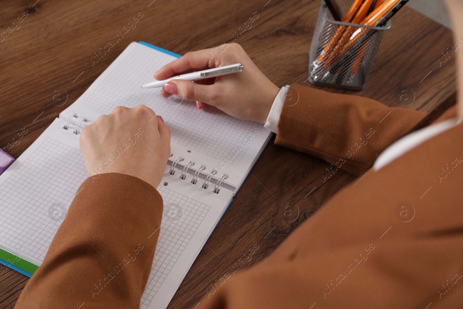 Photo of Woman taking notes at wooden table, closeup