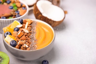 Photo of Bowl of delicious fruit smoothie with fresh orange slices, blueberries and granola on white table, closeup. Space for text