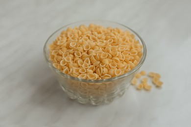 Photo of Bowl with uncooked conchiglie pasta on white marble table