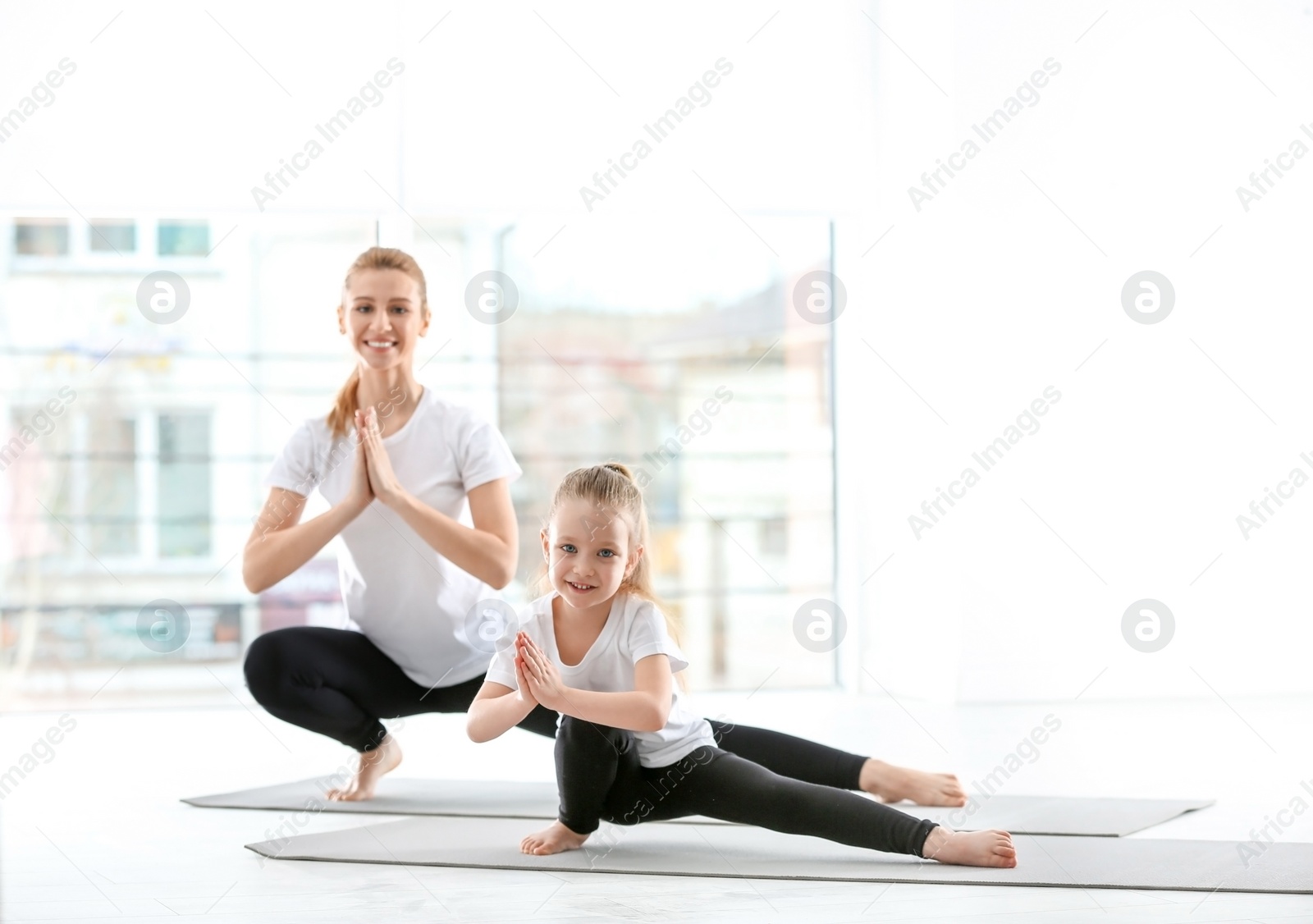 Photo of Mother and daughter in matching sportswear doing yoga together at home