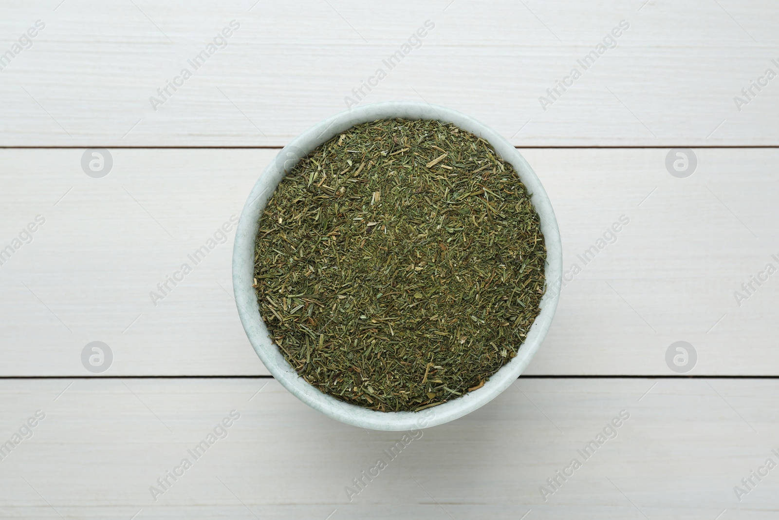 Photo of Dried dill in bowl on white wooden table, top view