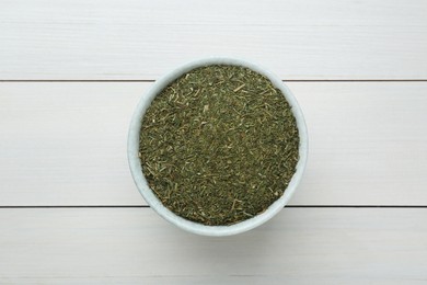 Photo of Dried dill in bowl on white wooden table, top view