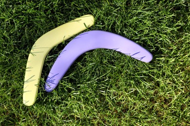Violet and yellow wooden boomerangs on green grass outdoors, above view