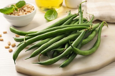 Board with fresh green beans on white wooden table