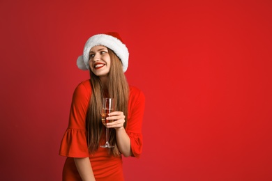 Photo of Young beautiful woman in Santa hat with glass of champagne on color background. Christmas celebration