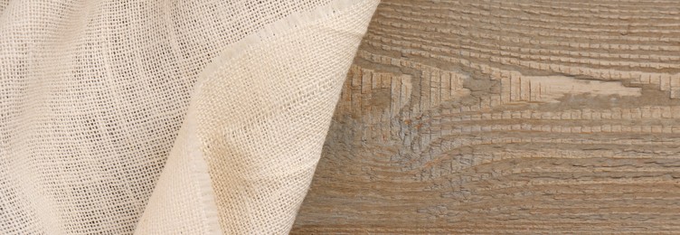 Beige burlap fabric on wooden table, top view. Space for text