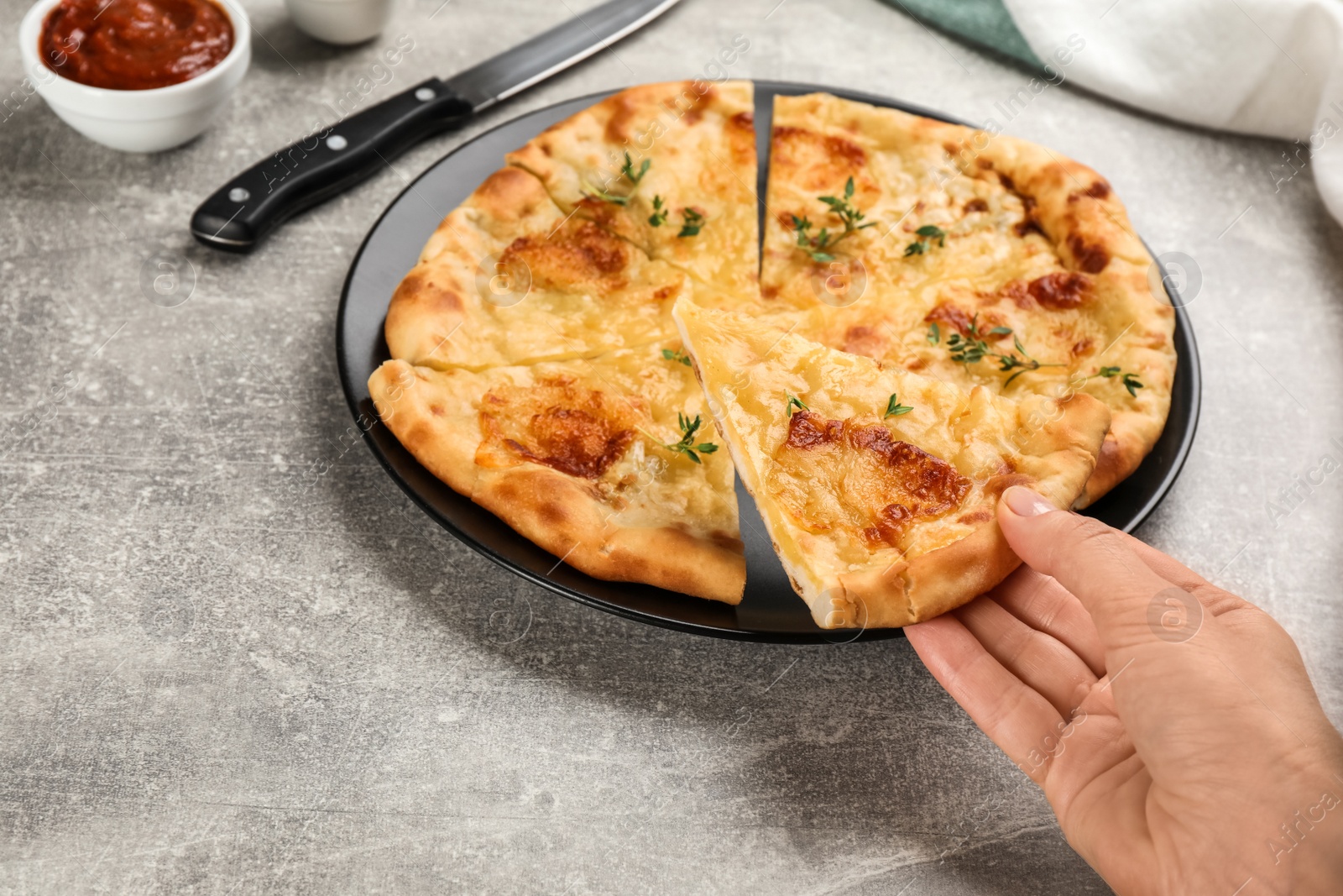 Photo of Woman taking piece of delicious khachapuri with cheese and thyme at light grey table, closeup