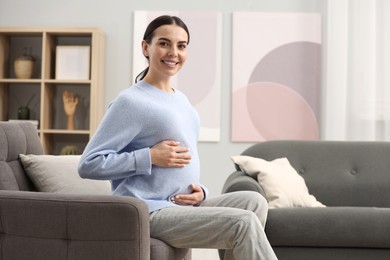 Photo of Happy pregnant woman on armchair at home, space for text