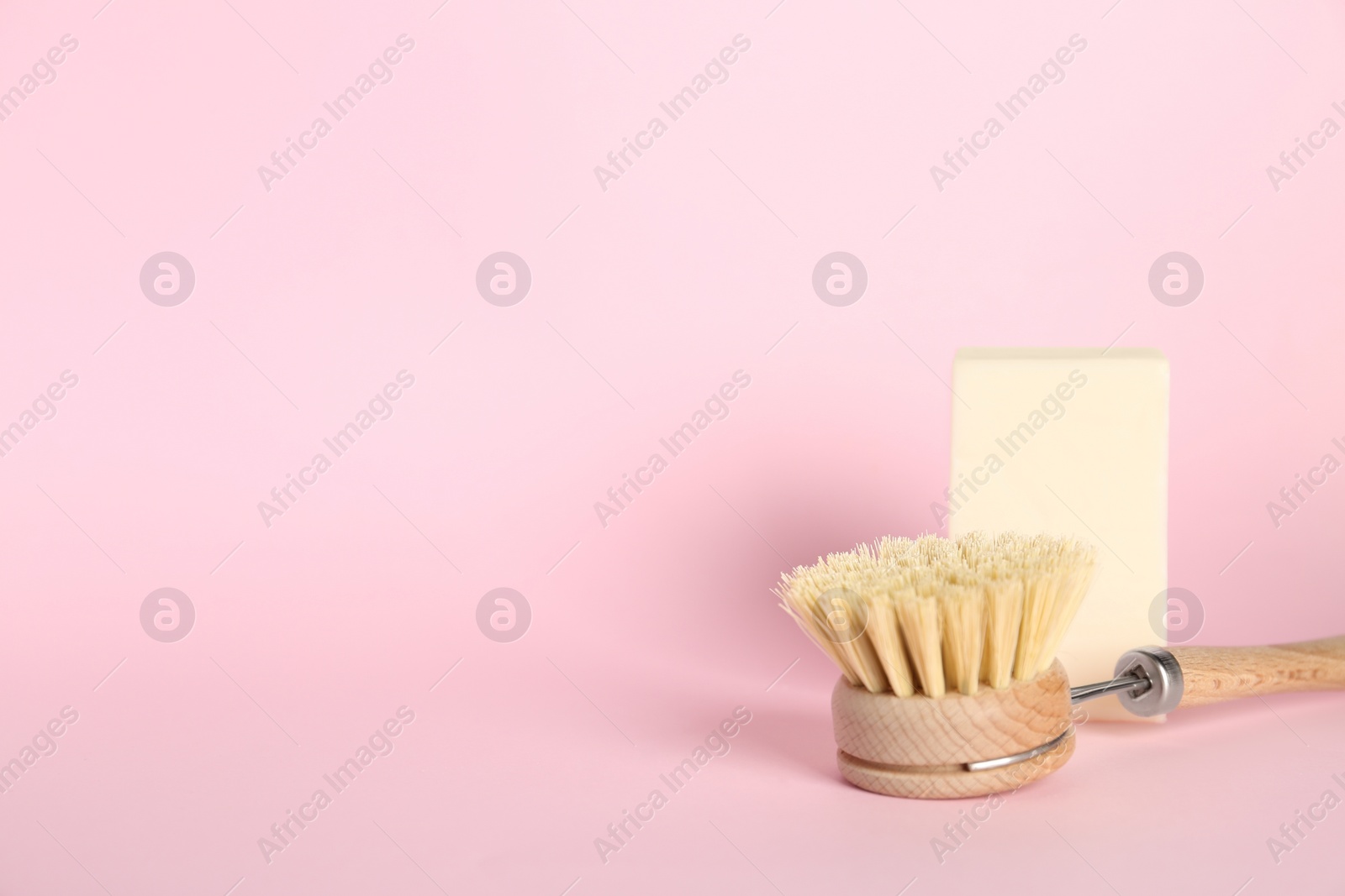 Photo of Cleaning brush and soap bar on pink background, space for text. Dish washing supplies