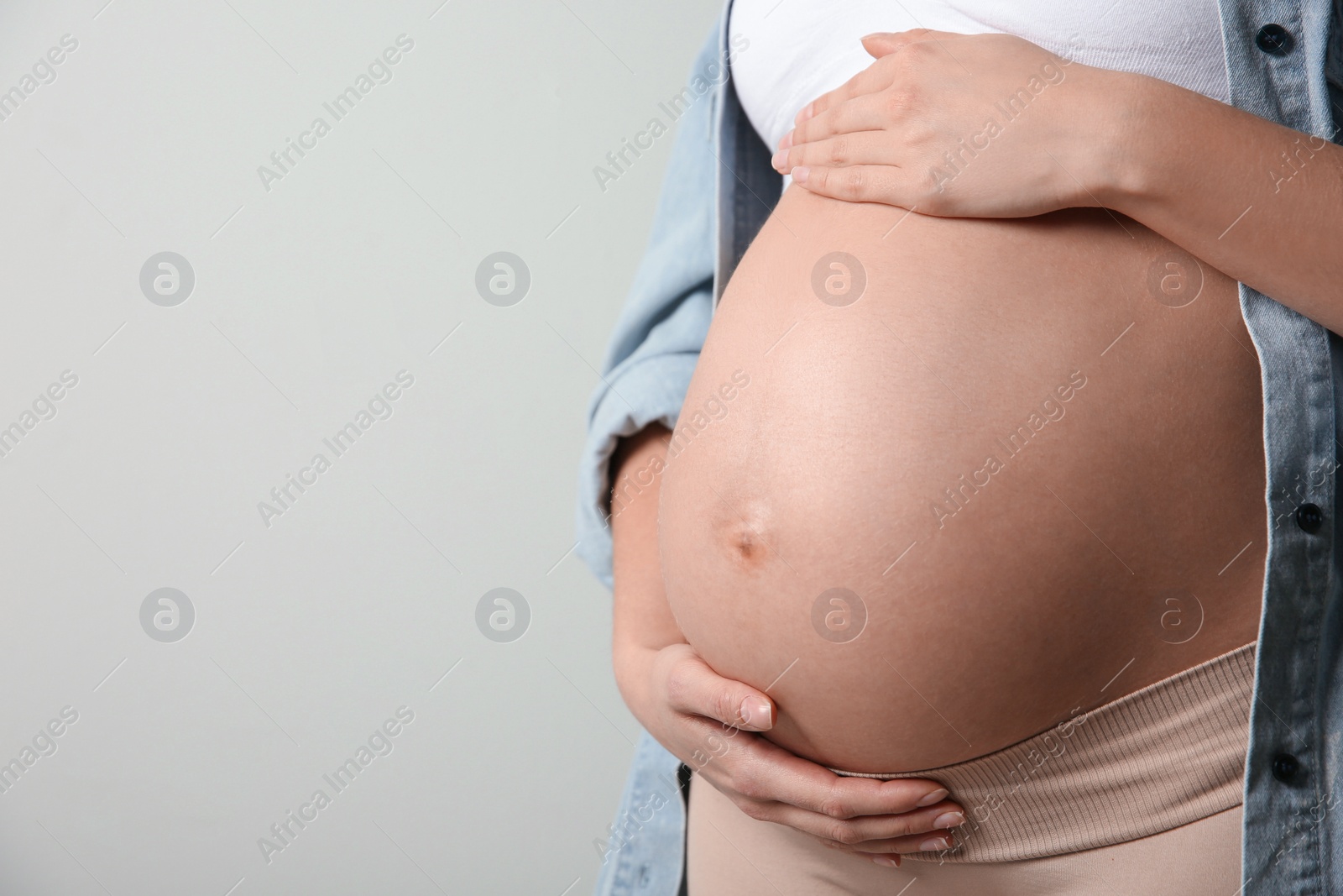 Photo of Pregnant woman touching her belly on light grey background, closeup. Space for text