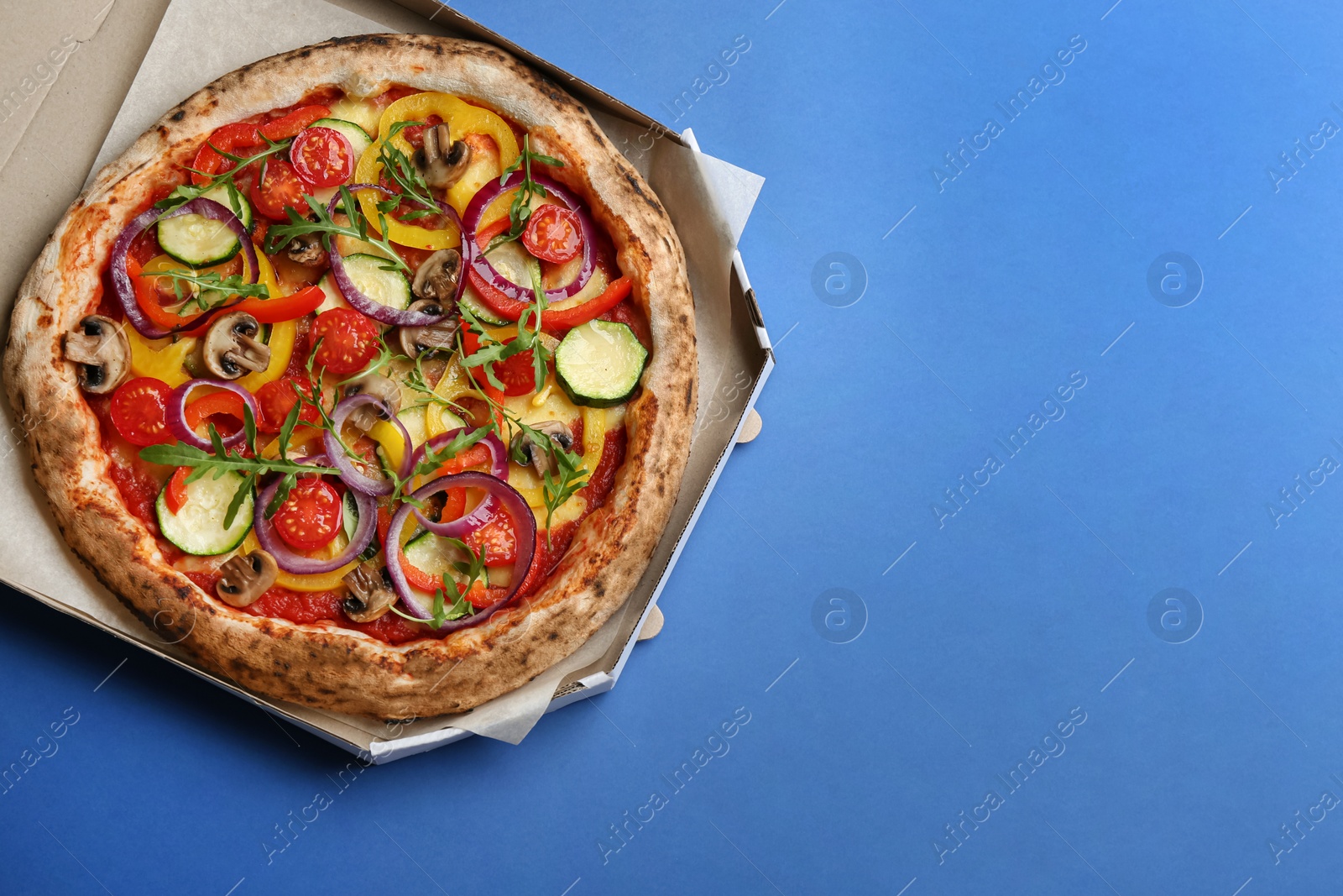 Photo of Delicious vegetable pizza in cardboard box on blue background, top view. Space for text