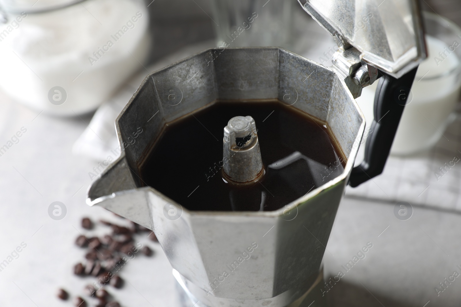 Photo of Brewed coffee in moka pot and beans on light grey table, closeup