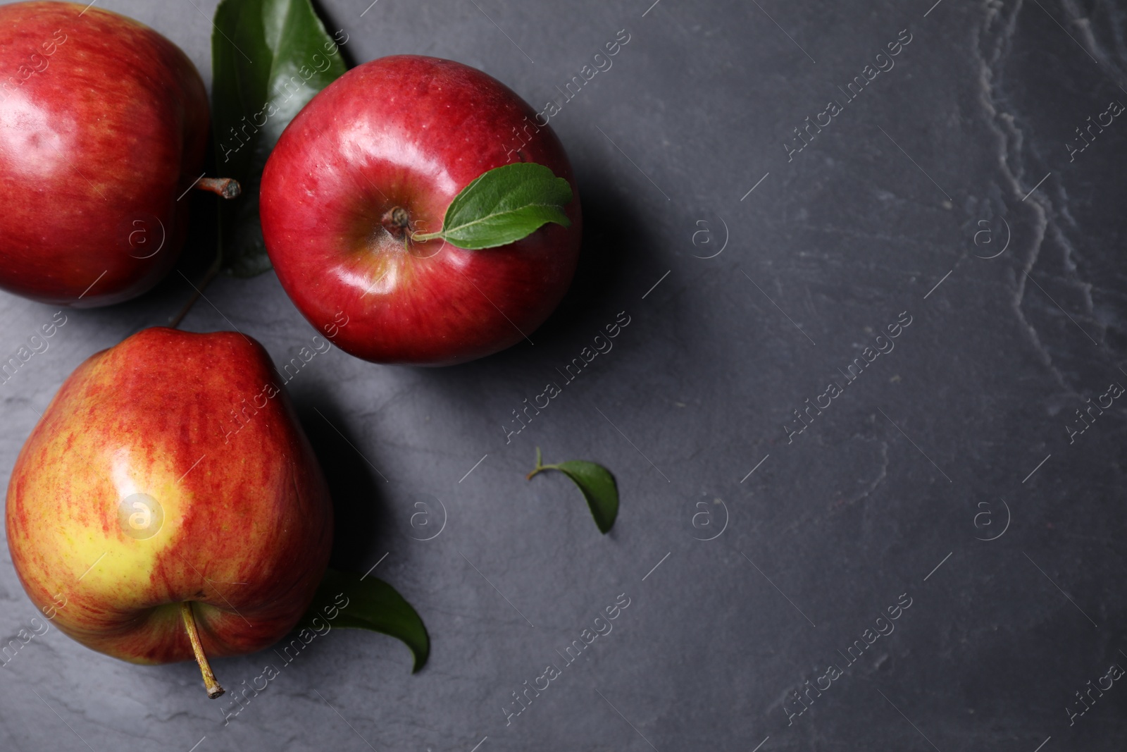 Photo of Ripe red apples and leaves on black textured table, flat lay. Space for text