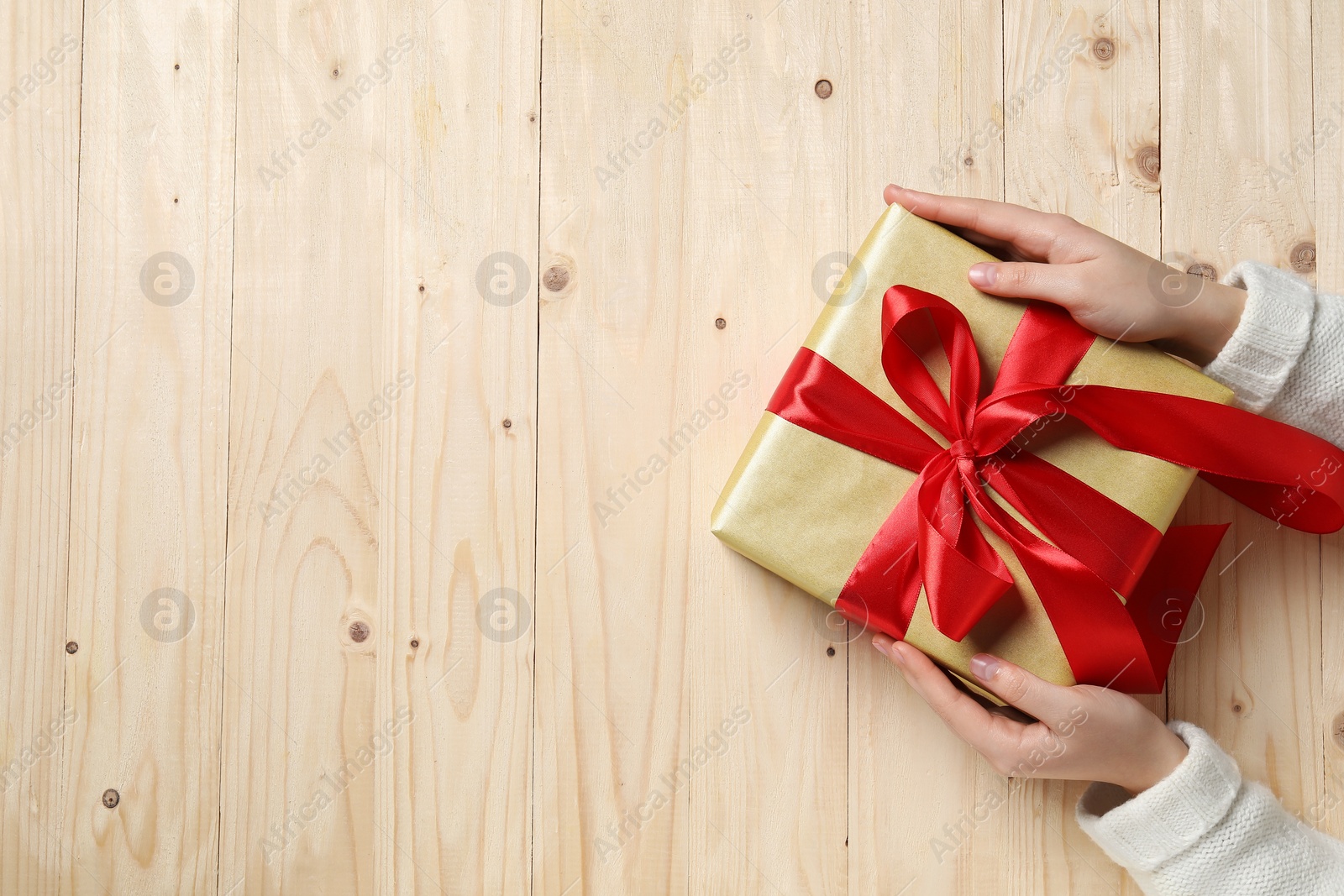 Photo of Christmas present. Woman holding gift box at wooden table, top view. Space for text