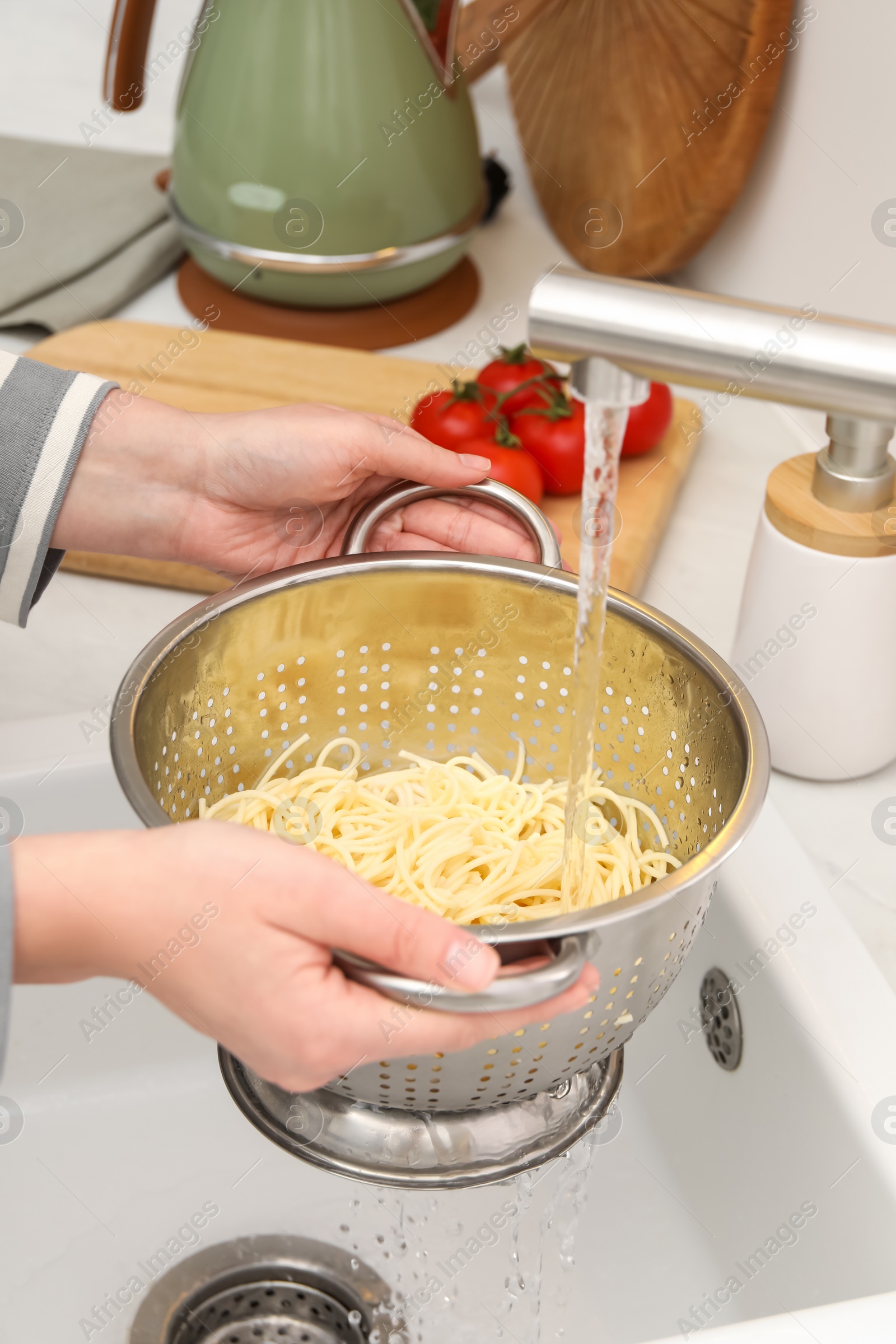 Photo of Woman rinsing pasta in colander above sink, closeup