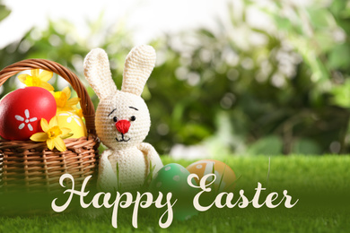 Image of Colorful eggs, toy rabbit on green grass with text Happy Easter