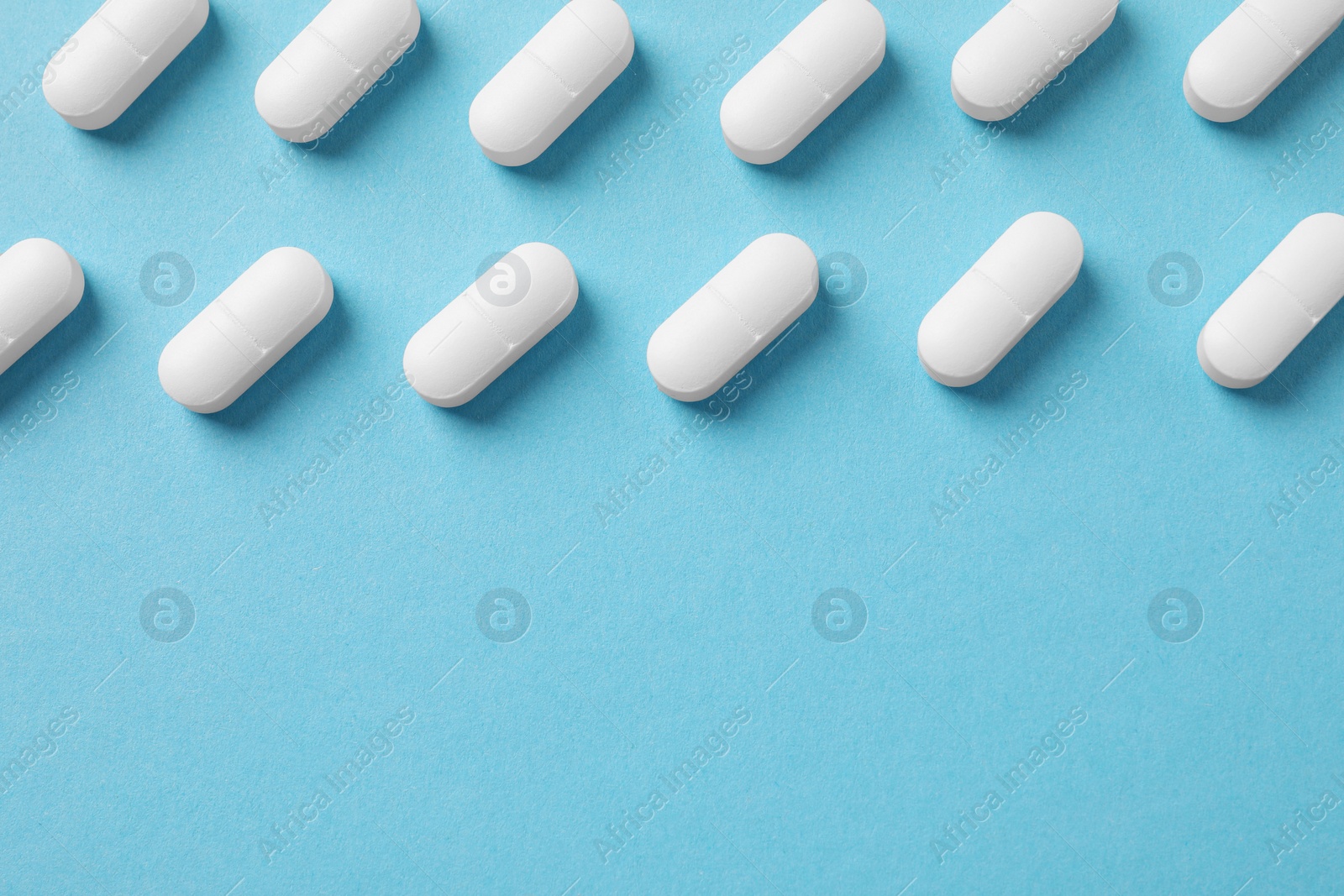 Photo of White pills on light blue background, flat lay. Space for text