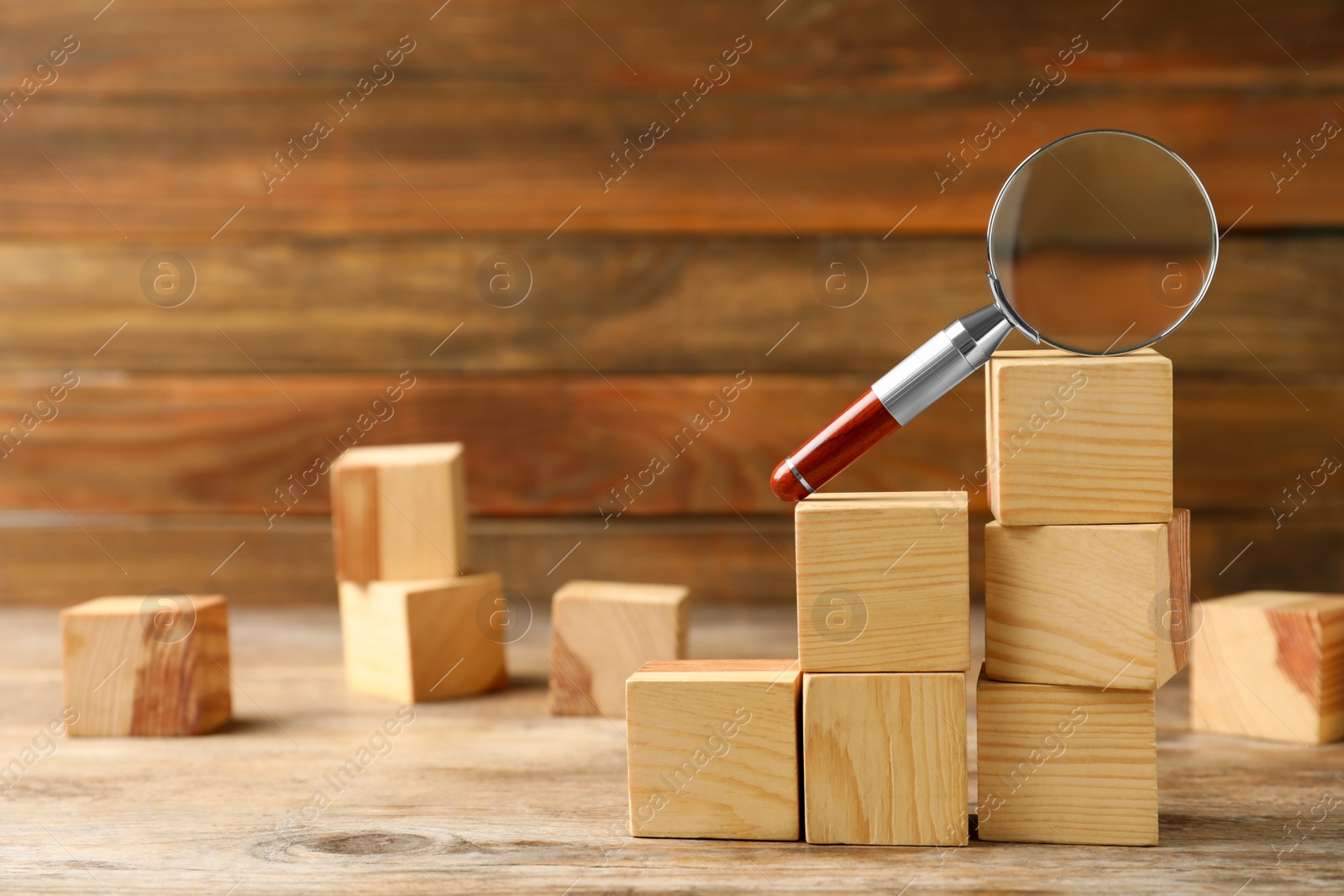 Photo of Magnifier glass and stairs made with cubes on wooden background, space for text. Find keywords concept