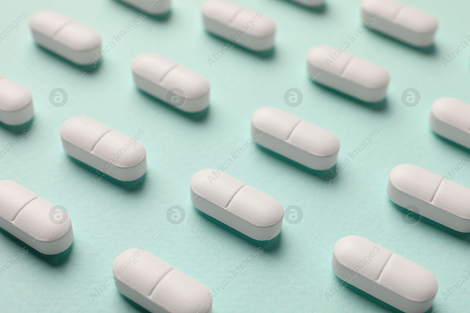 Photo of Many white pills on mint background, closeup