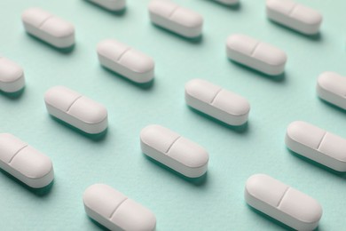 Photo of Many white pills on mint background, closeup