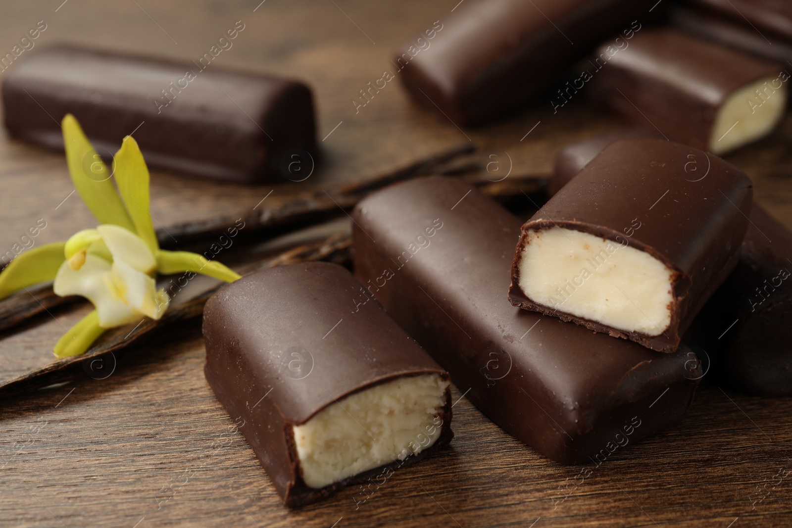 Photo of Glazed curd cheese bars, vanilla pods and flower on wooden table, closeup