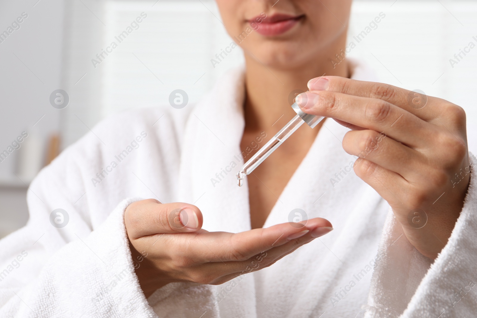 Photo of Woman applying cosmetic serum onto her hand on light background, closeup