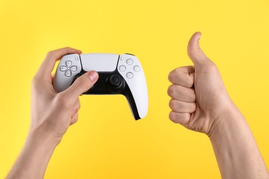 Photo of Man using wireless game controller and showing thumbs up on yellow background, closeup