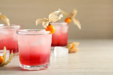 Refreshing cocktail decorated with physalis fruits on wooden table. Space for text