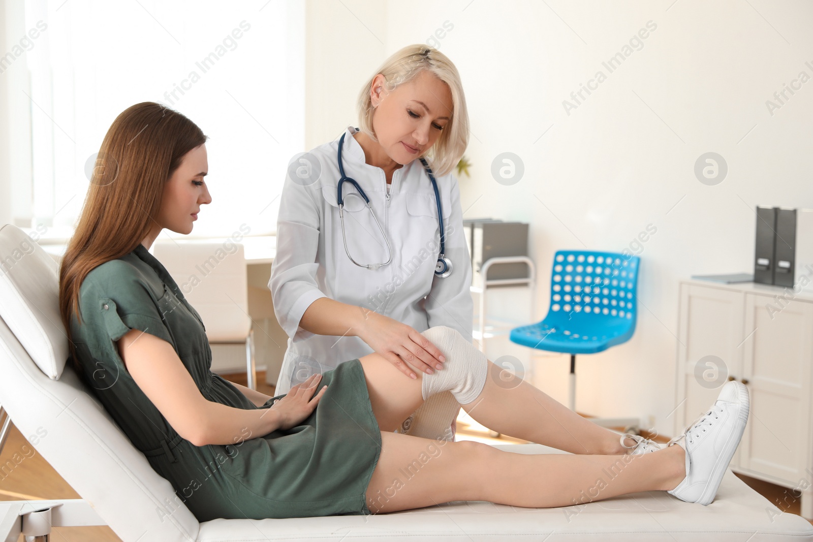 Photo of Doctor applying bandage to patient's knee in clinic