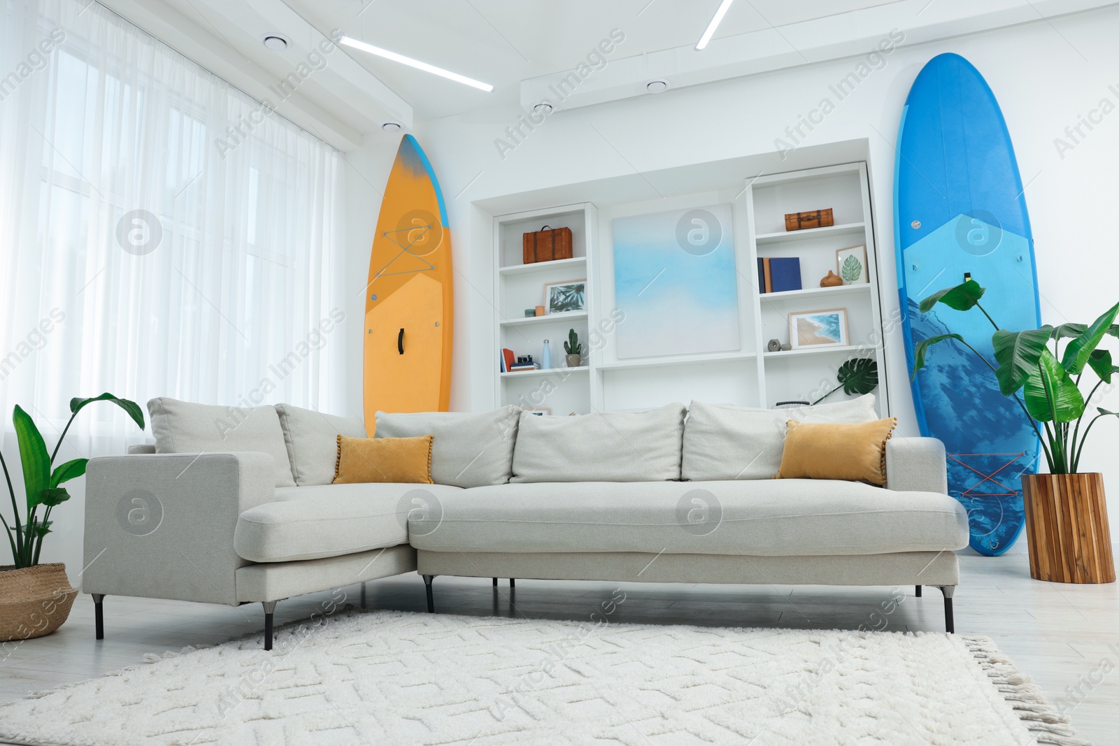 Photo of SUP boards, shelving unit with different decor elements and stylish sofa in room. Interior design