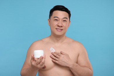 Photo of Handsome man applying body cream onto his chest on light blue background